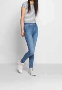 Jeans de mezclilla azules ajustados con una cintura de altura media, combinados con una camiseta de rayas grises y blancas de manga corta, y zapatillas blancas de caña alta.