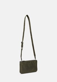 Bolsa cruzada de tecido verde com alça ajustável, fecho com zíper e logotipo em relevo. Textura suave com formato retangular.