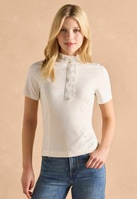 Bluză albă cu mânecă scurtă, cu guler volan și clapetă. Prezintă un accent cu nasturi, material moale și un design ajustat.