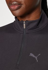 Svart sportskvart-zip-topp med en glatt tekstur og en subtil Puma-logo på brystet. Har en glidelås krage for justerbar dekning.