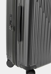 Maleta rígida de color gris oscuro con surcos verticales, cerradura de combinación integrada y ruedas negras suaves. Cuenta con un asa lateral para facilitar el transporte.