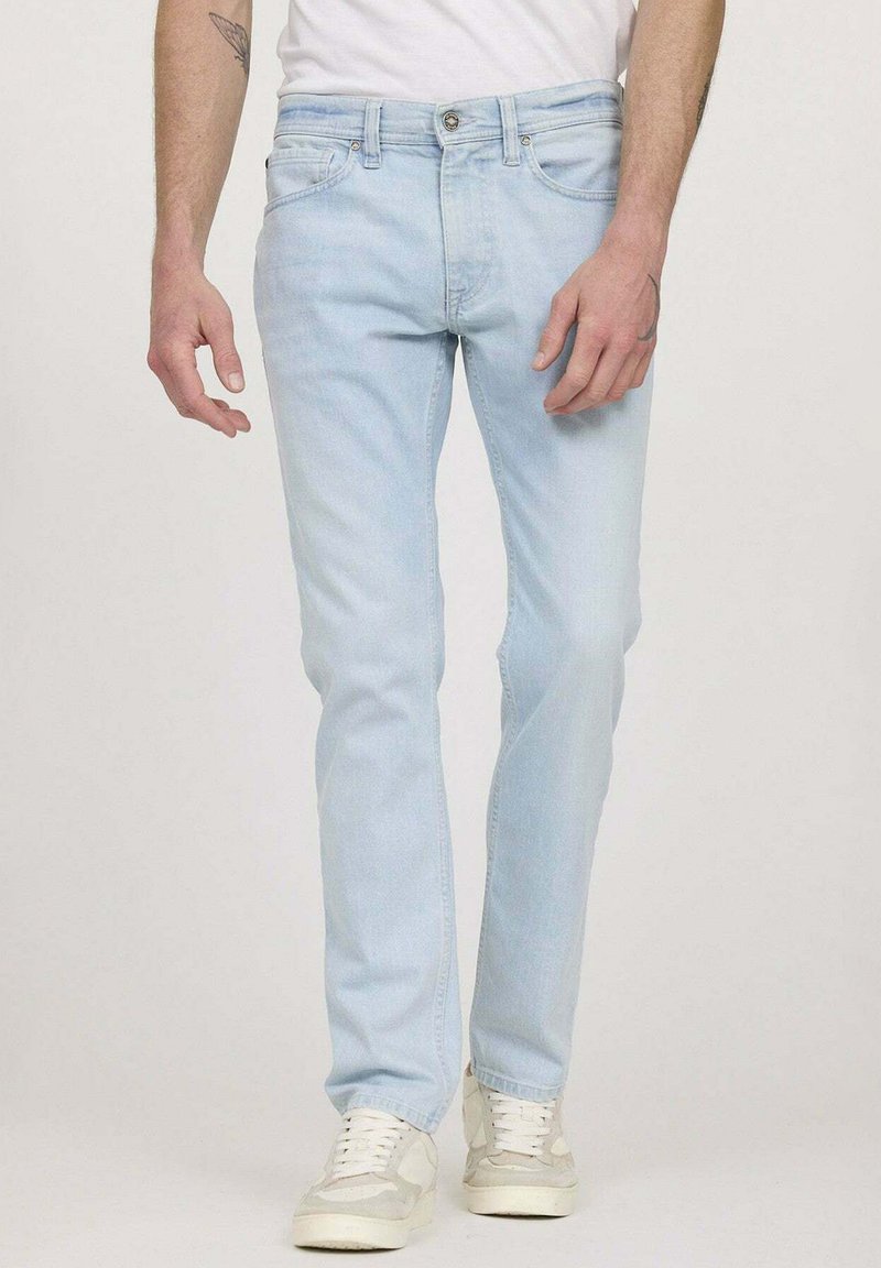 Jean en denim bleu clair avec une coupe droite, un design à cinq poches et un léger dégradé. Associé à des baskets blanc cassé pour le contraste.