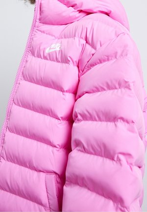 Doudoune rose avec logo Nike blanc sur la poitrine, design matelassé et détails visibles de la fermeture éclair et de la poche sur le côté.
