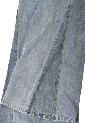 Panely ze světle a tmavě odstíněné džínové látky sešitá dohromady viditelnými švy, ukazující texturu a různé odstíny šedomodré.