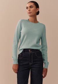 Muntgroene gebreide trui met een ronde hals en geribbelde manchetten, gecombineerd met donkere denim broek met hoge taille en zichtbare steken.