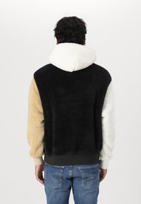 Hanorac din fleece cu culori variate: negru, crem și bej. Dispune de o glugă și o textură moale, cu margini și manșete ribbate.