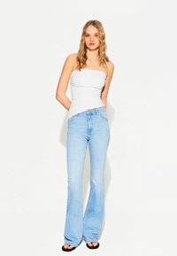 Top bianco senza spalline con design aderente, abbinato a jeans a zampa d'elefante blu chiaro. Textura liscia, estetica semplice, con una vestibilità comoda.