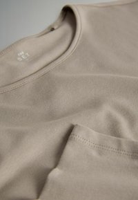 Tricou bej din bumbac cu guler rotund, textură subtilă și buzunar pe pieptul stâng. Tiv cusut și material neted.