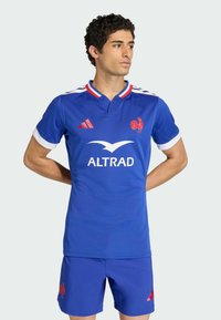 Modrý sportovní dres s krátkými rukávy, bílými manžetami a červeným límečkem. Obsahuje logo kohouta a značku ALTRAD, doplněný o odpovídající šortky.