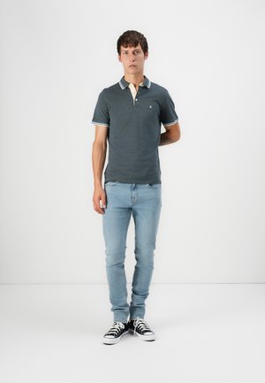 Donkergrijze polo met een witte en blauwe gestreepte kraag, gecombineerd met lichtblauwe jeans en zwarte sneakers met witte zolen. Slanke pasvorm.