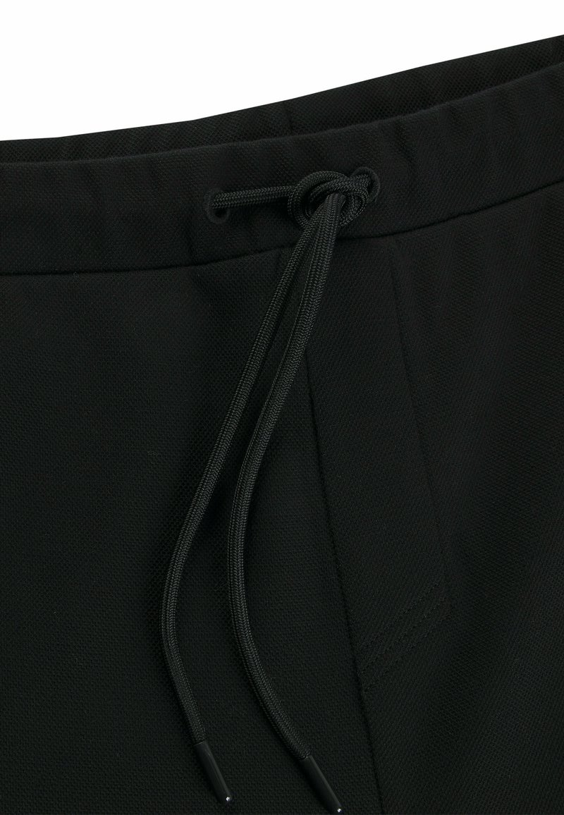 Pantalones cortos de tiro negro con cordón, hechos de una tela texturada. Cuentan con una cinturilla elástica, con lazos ajustables y un bolsillo lateral visible.