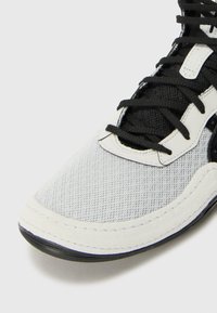 White mesh sneaker with black laces, rubber sole, and textured accents. Features a smooth suede overlay and stitched detailing.