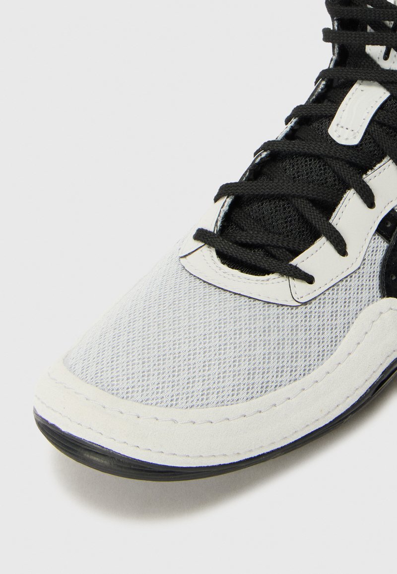 White mesh sneaker with black laces, rubber sole, and textured accents. Features a smooth suede overlay and stitched detailing.