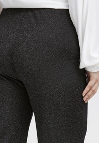 Svart, glittrande leggings med en mjuk textur, med hög midja och subtil lyster, i kombination med en vit topp med puffärmar.