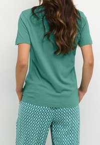Tyrkysové bavlněné tričko s krátkým rukávem a uvolněným střihem v kombinaci s vzorovanými tyrkysovými kalhotami s geometrickým vzorem.