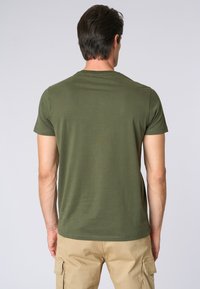 T-shirt verde oliva a maniche corte realizzato in cotone; presenta un collo rotondo e una vestibilità comoda. Tessuto uniforme senza motivi o grafiche visibili.