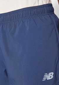 Marineblå sportshorts i slät tyg med elastisk midja; har en vit New Balance-logotyp på det nedre högra benet.