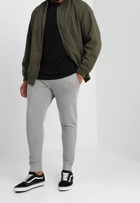 Chaqueta bomber verde con camiseta negra, pantalones de chándal gris ajustados y zapatillas negras con detalles blancos. Diseño minimalista y casual.