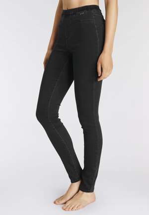 Black, stretchy denim pants with a high waistband, smooth texture, fitted design, and contrasting white stitching along the seams.