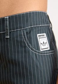 Șorturi dungi de culoare albastru marin cu dungi albe. Prezintă cusături albe, o buzunar frontal și o etichetă cu logo-ul Adidas pe talie.