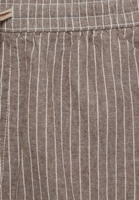 Tissu rayé marron avec de fines lignes blanches, présentant un tissage texturé et des plis en haut. Le matériau semble robuste et texturé.