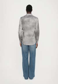 Grå langermet skjorte med subtile mønstre og knappemanchetter, sammen med lyseblå vidde denim jeans. Glatt stofftekstur.
