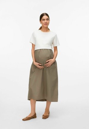 Maternity dress with a white top and olive green skirt, featuring a loose fit, stretchable waist, and flat brown shoes.