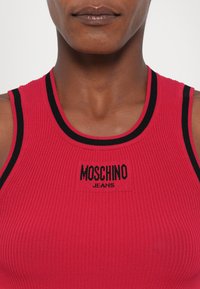 Raudonas juostuotas liemenėlė su juodu apvadu, centre esantis kvadratinis logotipas skaito "MOSCHINO JEANS". Lygus paviršius ir prigludusi forma.
