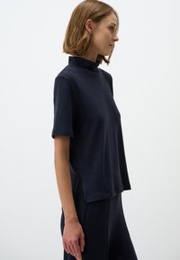 Maglietta blu navy a maniche corte con collo alto, realizzata in tessuto testurizzato, dotata di spacchi laterali per facilitare i movimenti. Design semplice.