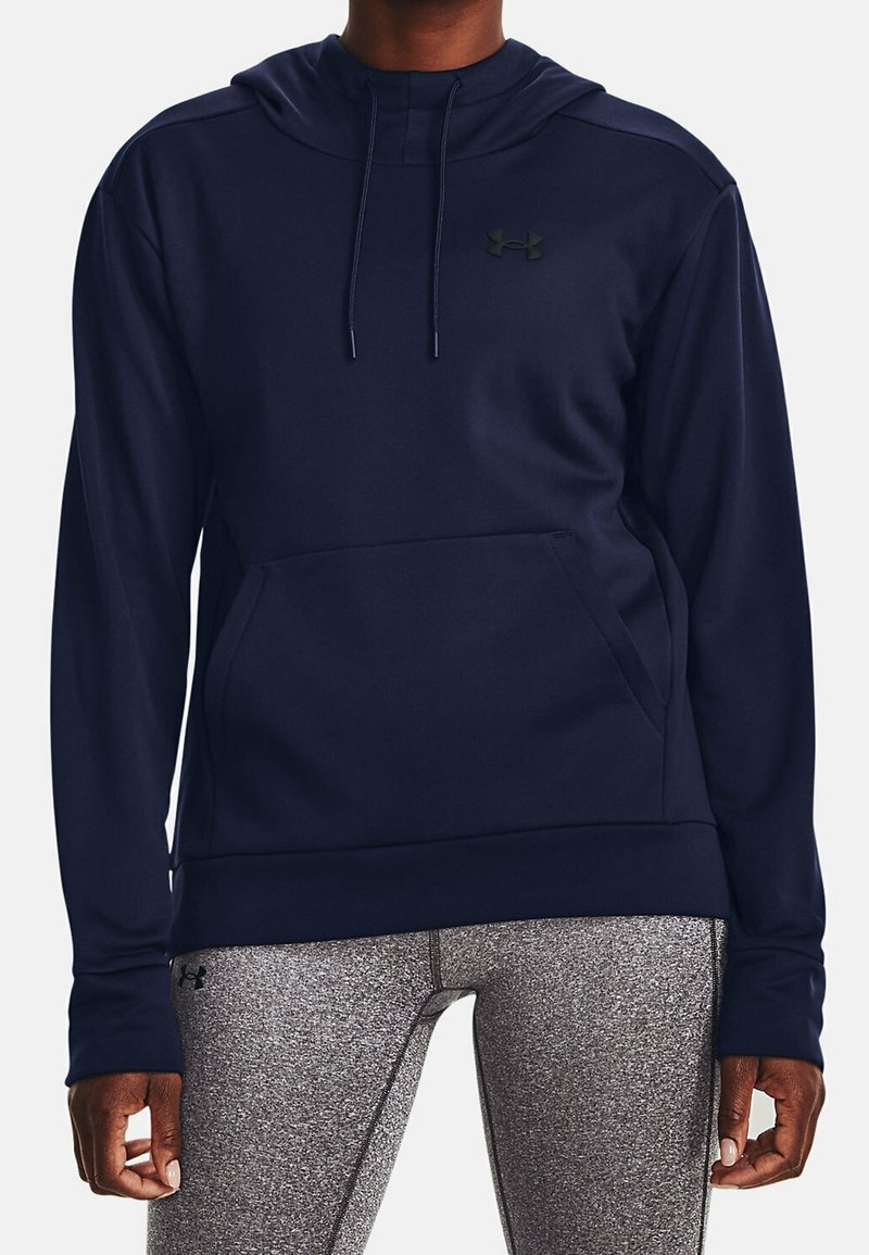 Personne portant un sweat à capuche bleu marine avec une poche avant et des leggings gris texturés, debout, les bras détendus le long du corps.