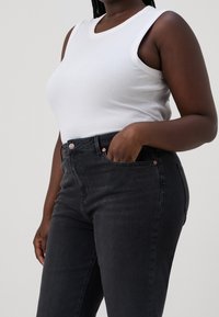 Top in cotone bianco a costine abbinato a jeans skinny in denim scuro. I jeans presentano una chiusura a bottone e discreet accessori in ottone.