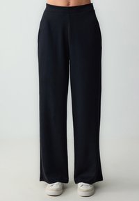 Zwarte wijde broek met een gladde textuur en elastische tailleband, met een rechte pasvorm en een lengte die tot op de grond valt.