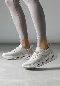 Bílé sportovní boty s texturovaným svrškem, síťovanými panely a masivní podrážkou s výřezy pro ventilaci a flexibilitu.