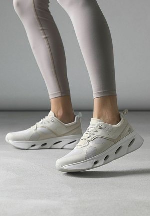 Scarpe da atletica bianche con una tomaia texturizzata, pannelli in rete e una suola spessa con ritagli per la ventilazione e la flessibilità.