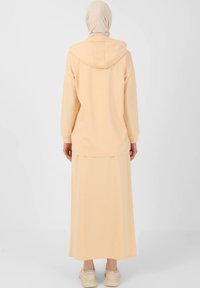 Peach-colored hoodie with a hood, long sleeves, and a relaxed fit, paired with a matching long skirt. Soft texture, simple design.