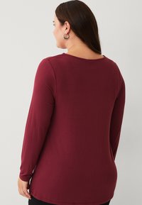 Maroon long-sleeve shirt with a rounded neckline, soft texture, and a relaxed fit, featuring side slits at the hem for added movement.