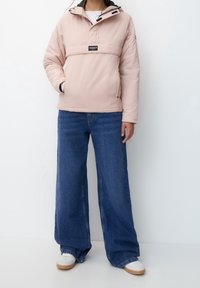 Helles rosa, gefüttertes Pullover-Jacke mit Kapuze, Halb-Reißverschluss vorne und Logopatch; kombiniert mit weit geschnittenen blauen Jeans und weißen Sneakers.