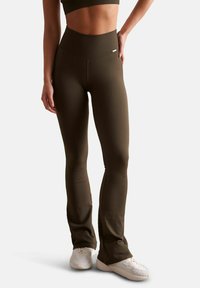 Leggings côtelés vert olive avec une taille haute, présentant une texture lisse et une conception évasée ; associés à des chaussures de sport blanches.