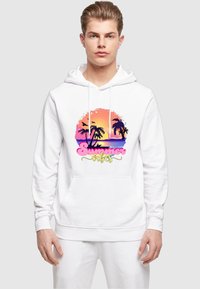 Felpa bianca con cappuccio che presenta una grafica colorata con un tramonto, palme e il testo "Vibes Estive" in rosa e giallo. Tessuto morbido, vestibilità casual.