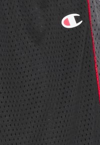 Svarta idrottsshorts i meshmaterial med en röd accentrand och en vit logotyp fram. Strukturerad yta med ventilationshål.