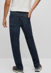 Džíny z tmavě modrého denimu s rovnými nohavicemi, pětikapsovým střihem a viditelnými švy. Lehká tkanina s hladkou texturou.