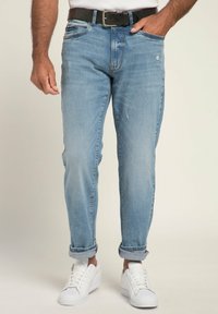 Vaqueros de mezclilla azul claro con un corte relajado, puños doblados, cinco bolsillos y un ligero desgaste, combinados con zapatillas blancas y un cinturón negro.