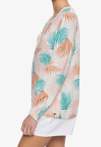 Camicia a maniche lunghe realizzata in tessuto leggero, con una stampa di foglie di palma rosa e teal. Dettaglio in pizzo al collo e polsini con bottoni.