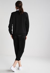 Sudadera negra de manga larga, con puños y dobladillo acanalados, combinada con pantalones cortos negros texturizados y zapatillas blancas.