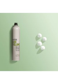 Spray volumizzante KMS in una lattina metallica cilindrica, argento con testo verde, accanto a quattro palle di schiuma bianche, su uno sfondo verde pallido.