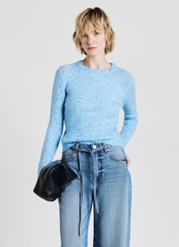 Pull en tricot bleu clair avec un col rond et une texture mouchetée, associé à un jean en denim taille haute et ample, ainsi qu'un sac pochette noir.