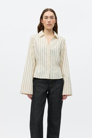 Koszula na guziki w paski w kolorze kremowym i czarnym, z dekoltem w serek, długimi rozkloszowanymi rękawami i dopasowaną talią. Połączona z ciemnymi dżinsami.