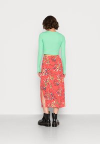 Haut à manches longues cropped vert menthe associé à une jupe midi à imprimé floral corail avec des fentes, porté avec des bottines à talons en vernis noir.