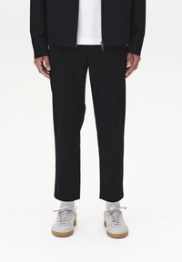 Czarne, zwężane spodnie o gładkiej fakturze, zestawione z szarymi sneakersami. Strój cechuje się czystym, minimalistycznym designem.