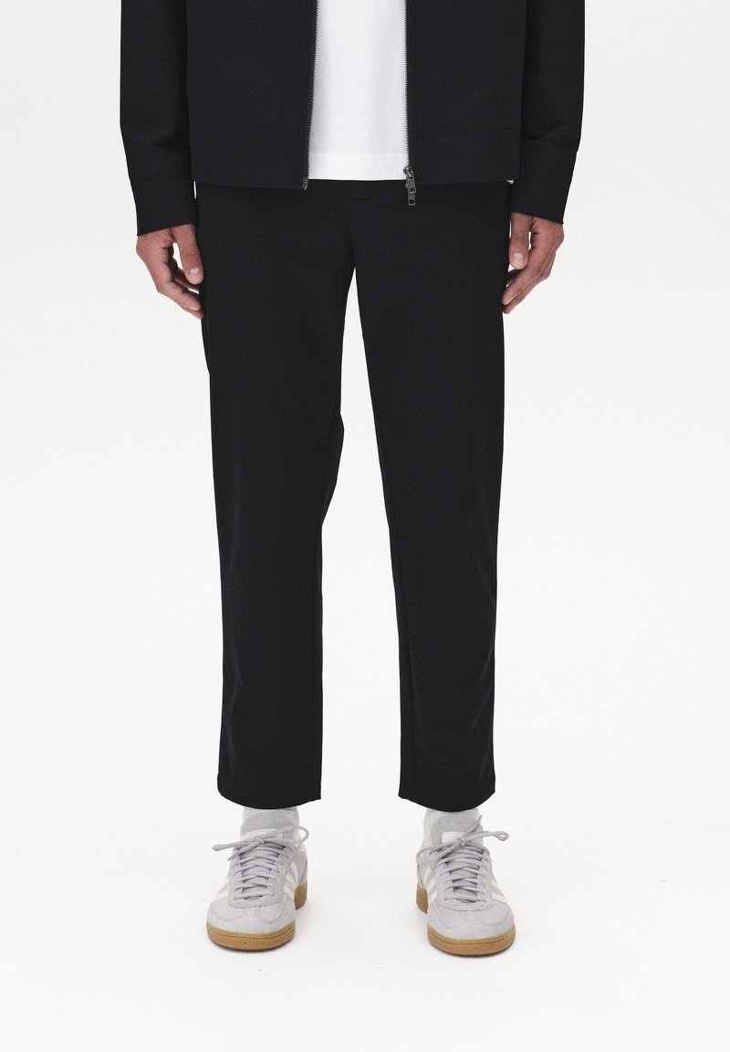 Czarne, zwężane spodnie o gładkiej fakturze, zestawione z szarymi sneakersami. Strój cechuje się czystym, minimalistycznym designem.